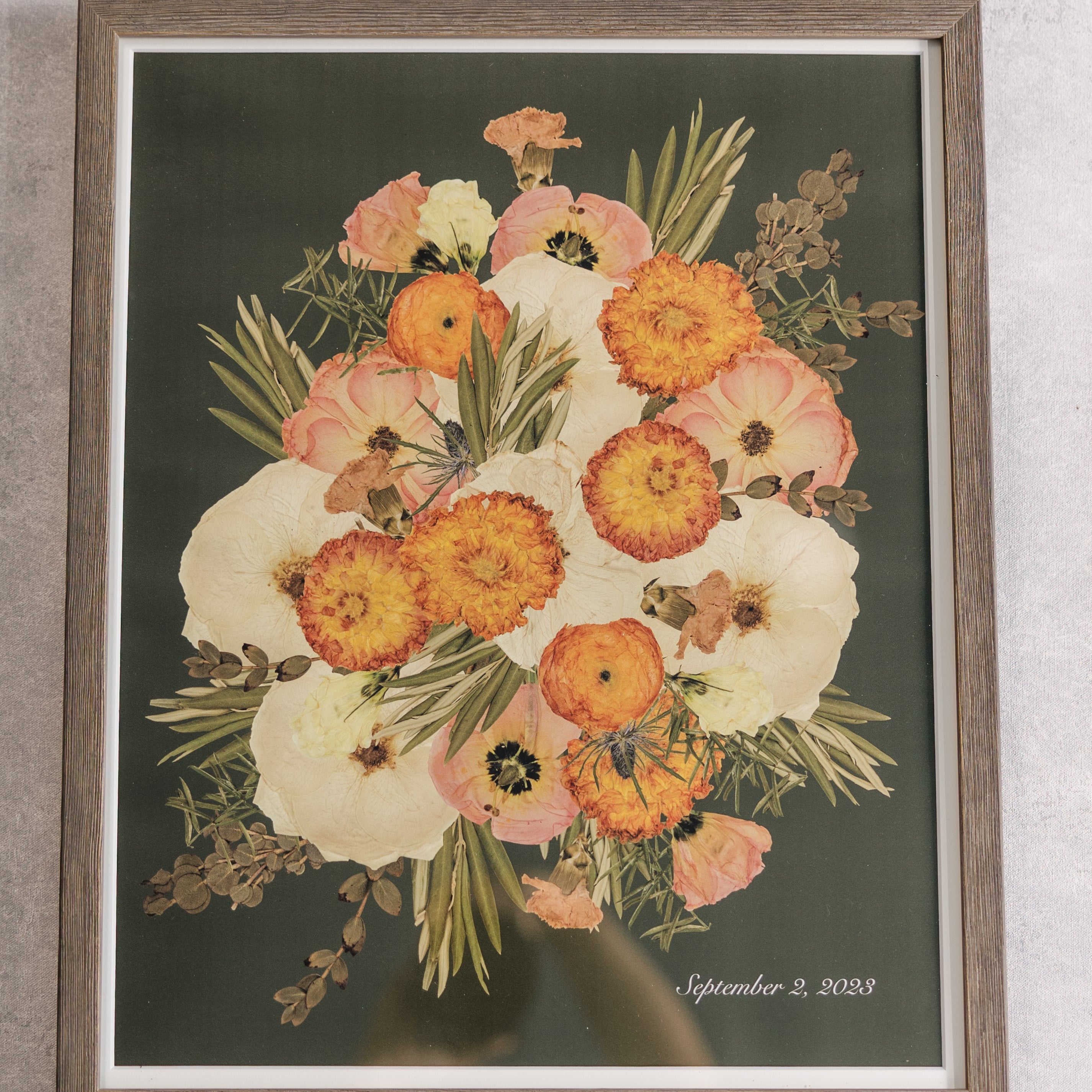 A large brown frame with orange and white pressed florals against a green background with a date that reads September 2, 2023