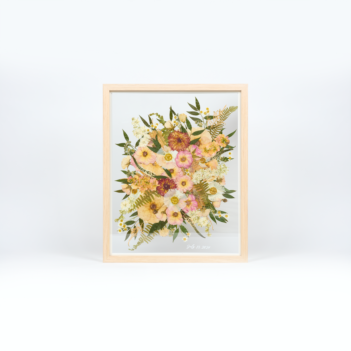 Bridal bouquet preservation in a 16x20 natural wood frame. Pink, coral, white, and green pressed florals fill the frame with a floating glass background. A dainty vinyl date addition accents the bottom right corner of the frame.