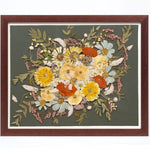 A walnut wood frame with preserved flowers encased on top of a dark green background