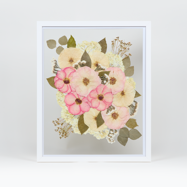 A pressed bridal bouquet in a white wood floating frame featuring pressed pink and white florals.