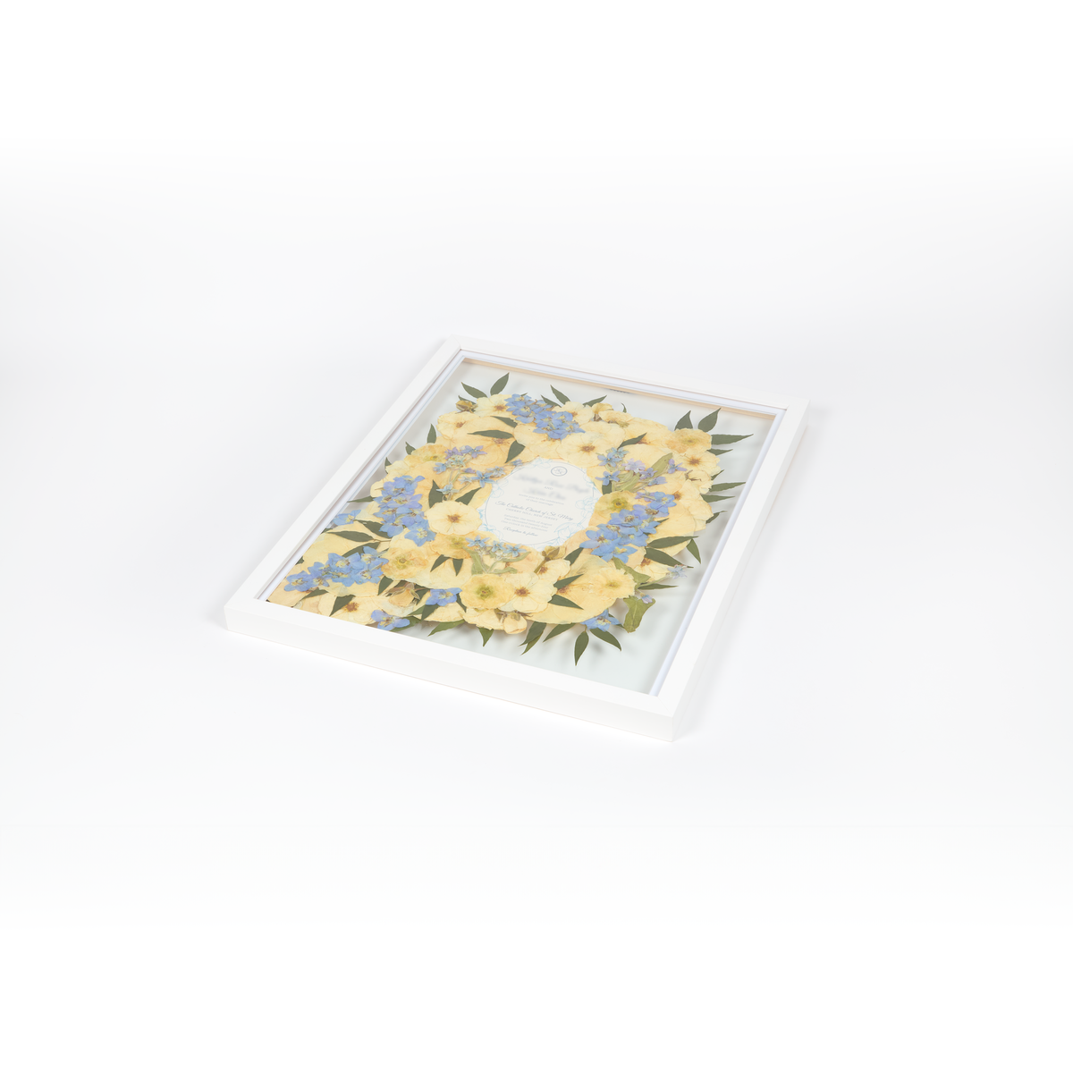 Floral preservation pressed flower frame with white and blue pressed florals. 16x20 white wood frame bridal bouquet preservation design featuring a wedding invitation in the center.