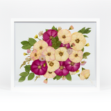 A pressed bridal bouquet in a white wood floating frame featuring pressed pink, red, and white florals with a preserved boutonniere in the corner.