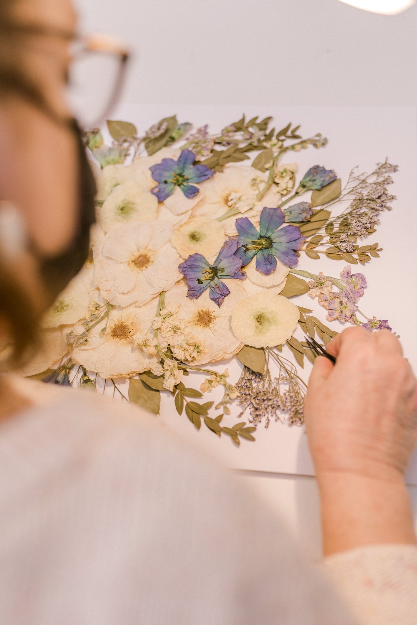 A person using tweezers to work on a pressed floral design