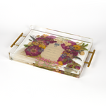 A pressed flower resin serving tray with vibrant colorful flowers and an invitation in the center. Wedding bouquet preservation as functional home decor.