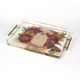 A pressed flower resin serving tray with vibrant colorful flowers and an invitation in the center. Wedding bouquet preservation as functional home decor.