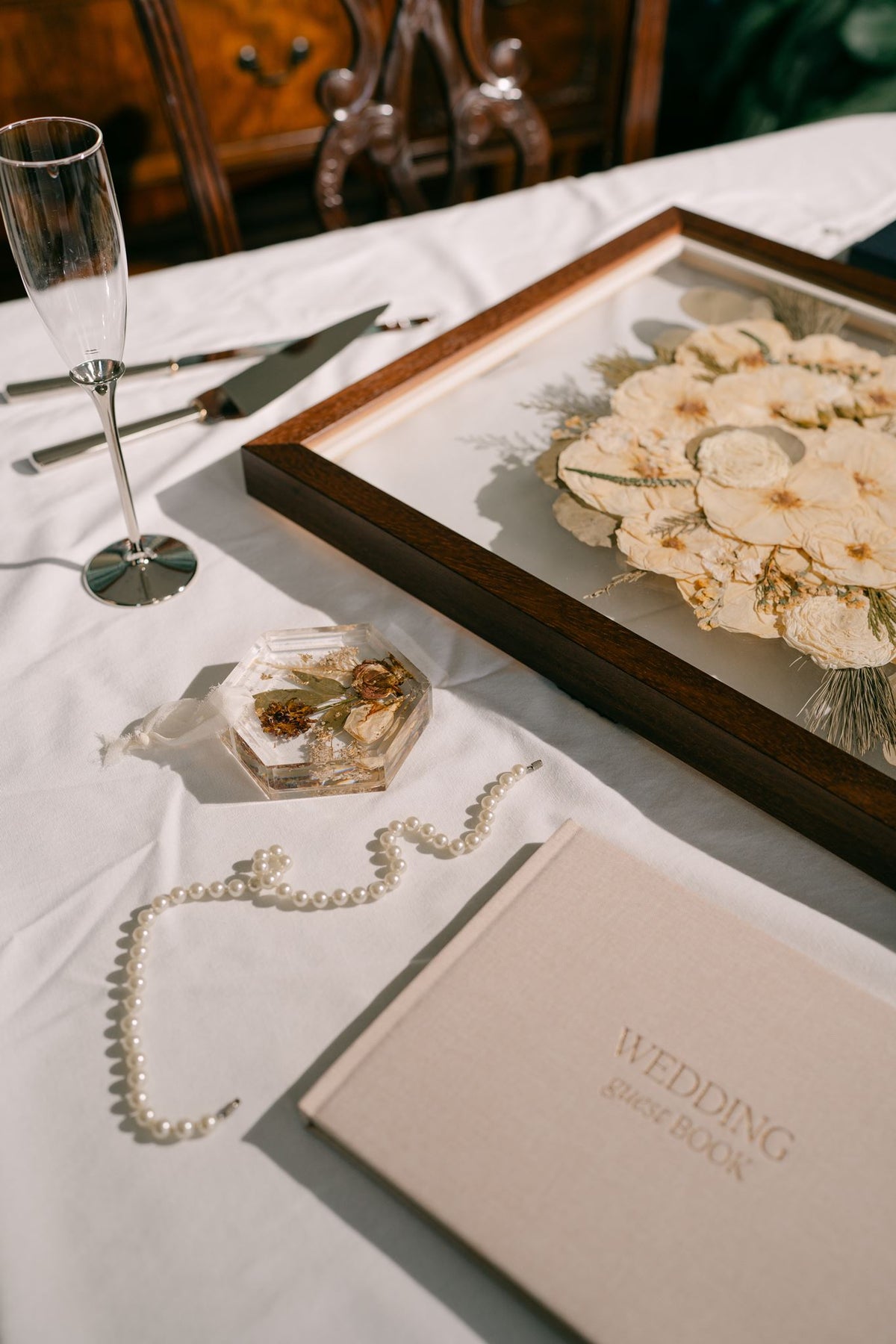 Hardcover wedding guest book in beige from Element Marketplace, shown on a table with pressed floral products, frame and coaster, and a champagne flute