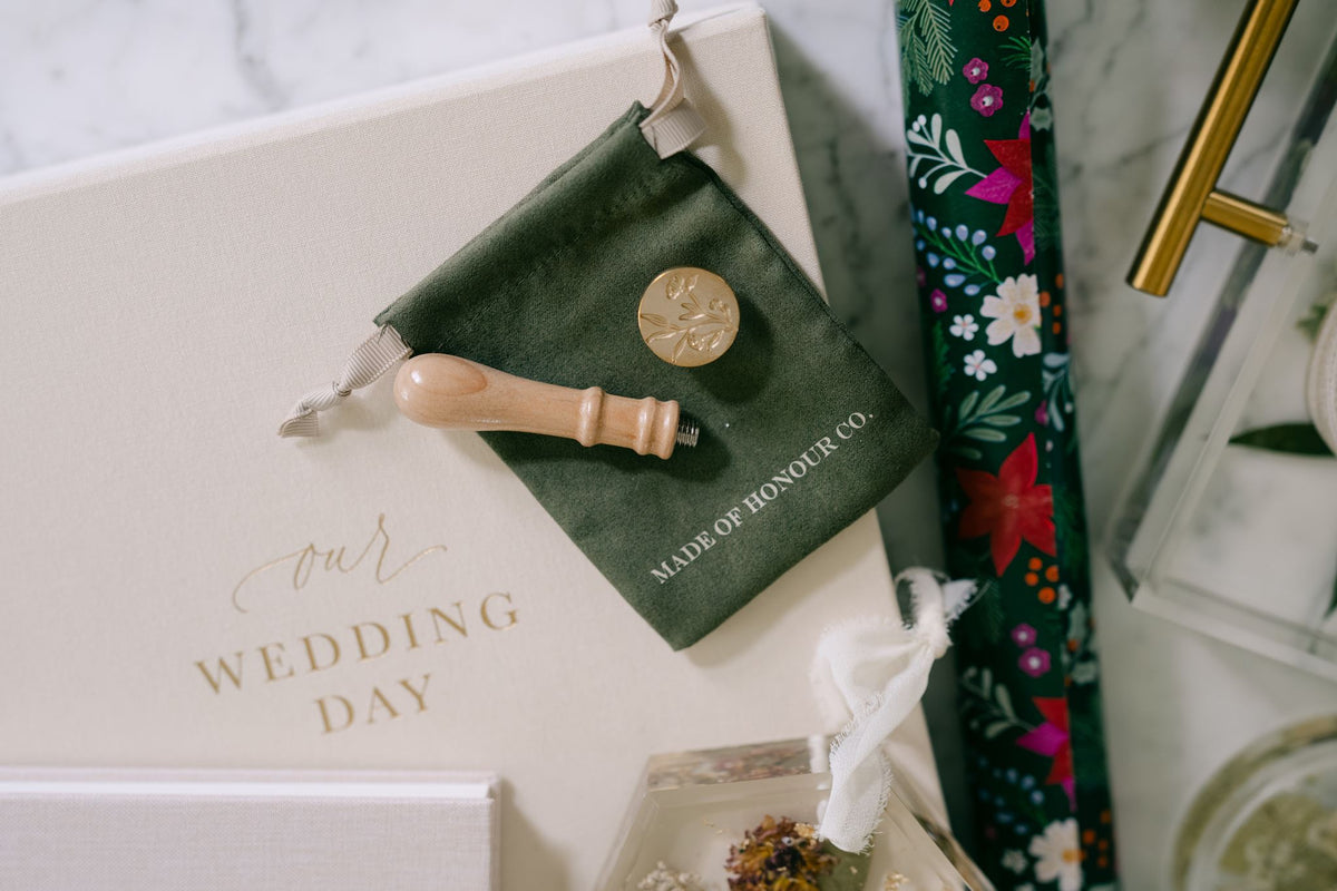Brass wildflower wax seal stamp from Element Marketplace, shown separated on a cleaning cloth, and wedding day album.