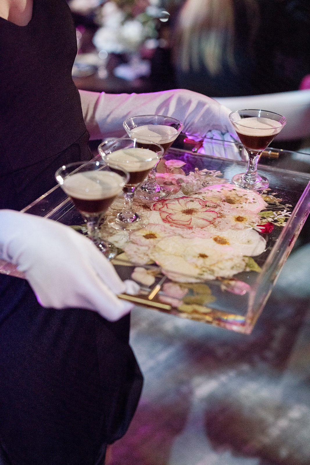 a person holding a serving tray with pressed flowers holding beverages