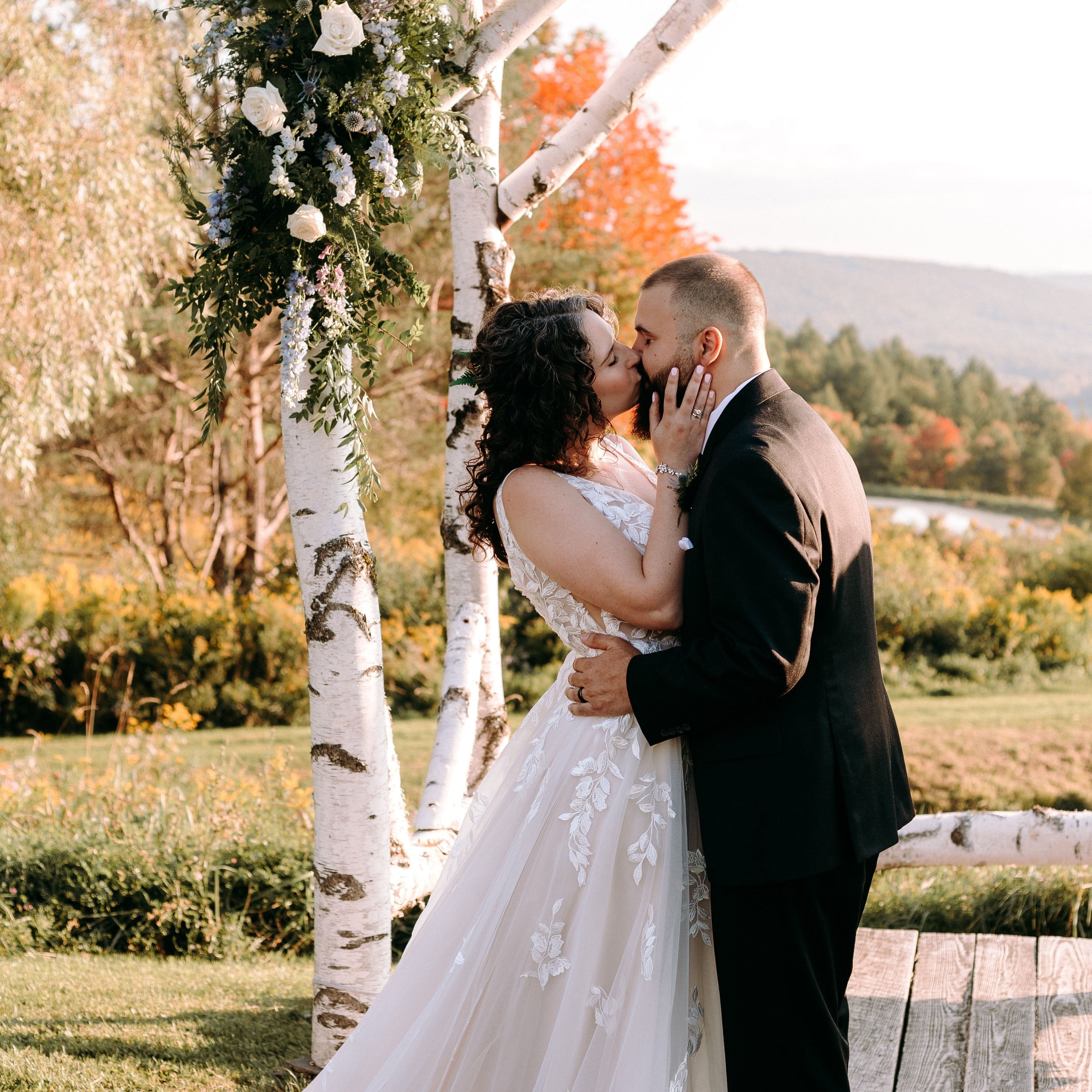 a bride and groom kissing under an altar filled with florals outside