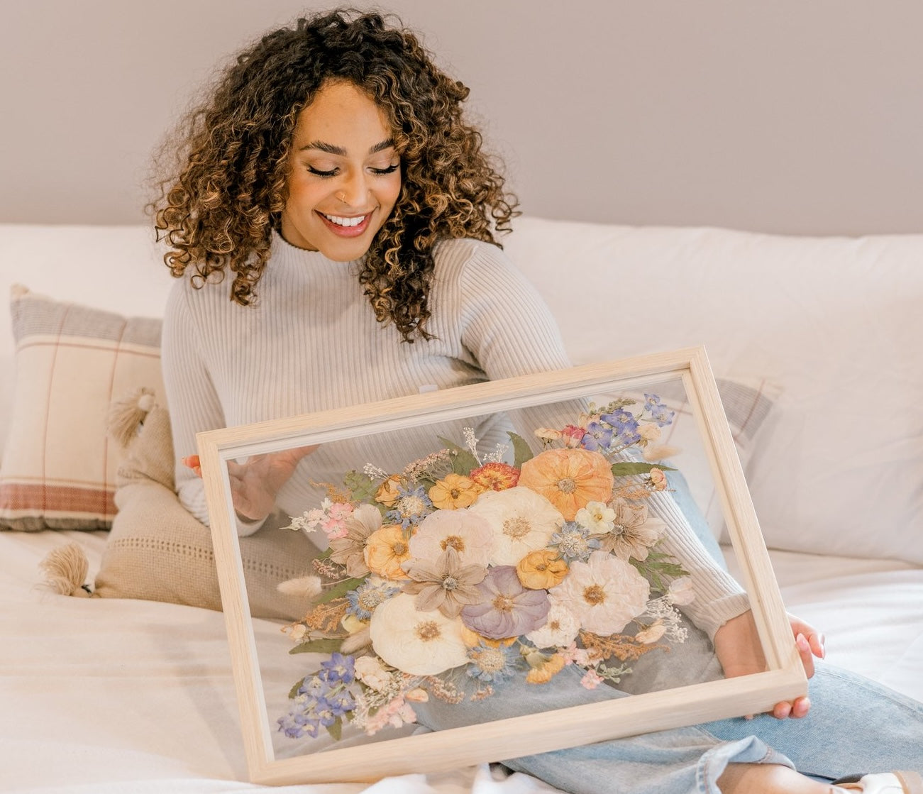 a woman holding a large tan frame with pressed flowers in a bed