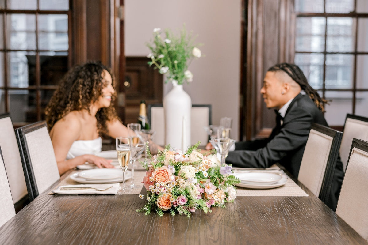 colorful bouquet on a wood table in front of a happy bride and groom holding hands