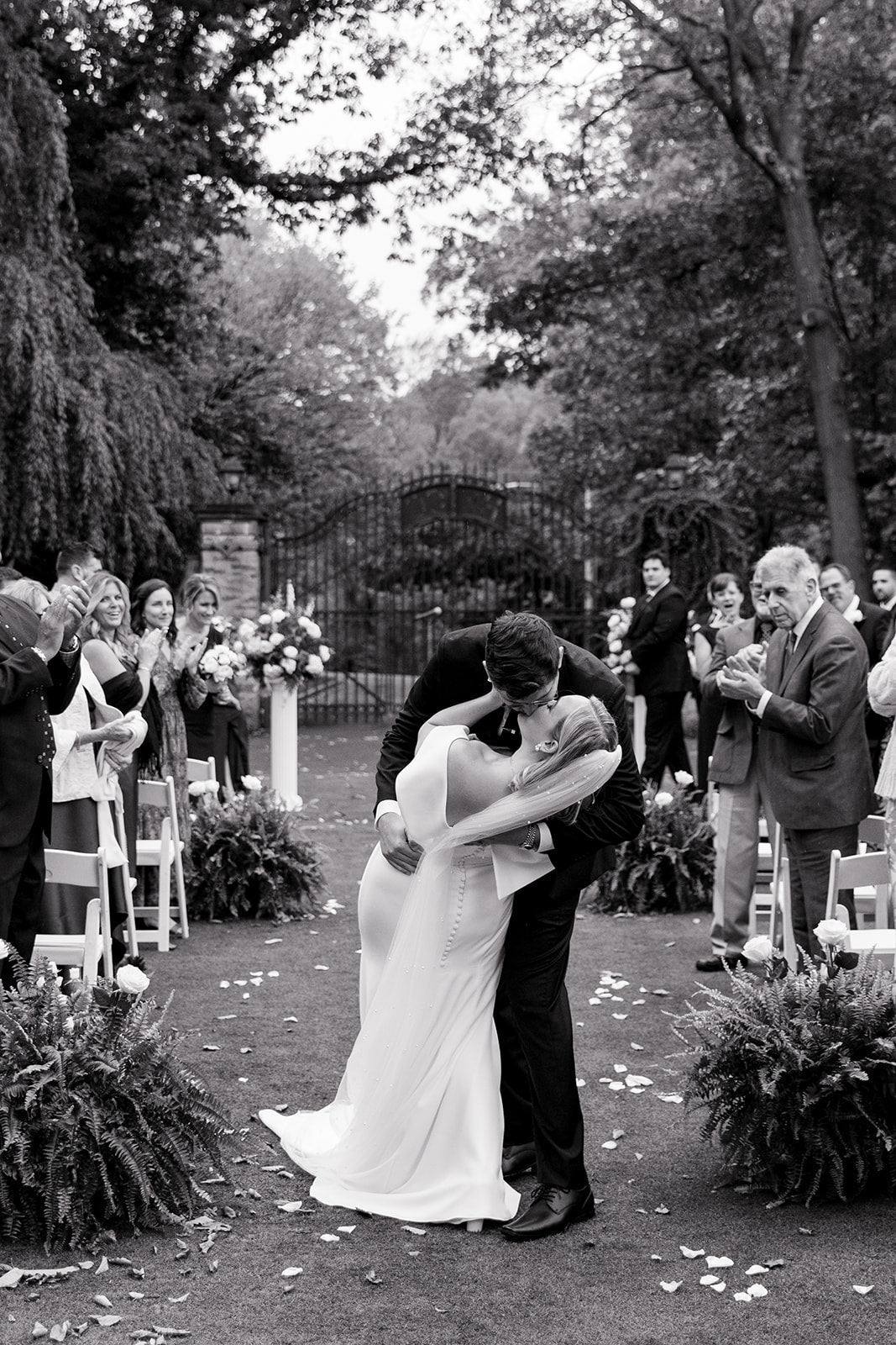 black and white photo of a bride and groom kissing down the aisle