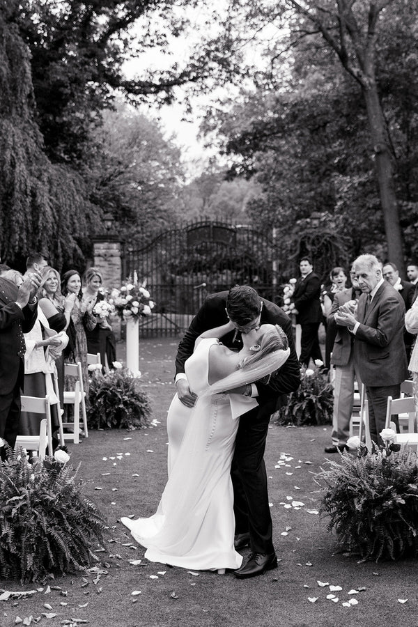 black and white photo of a bride and groom kissing down the aisle