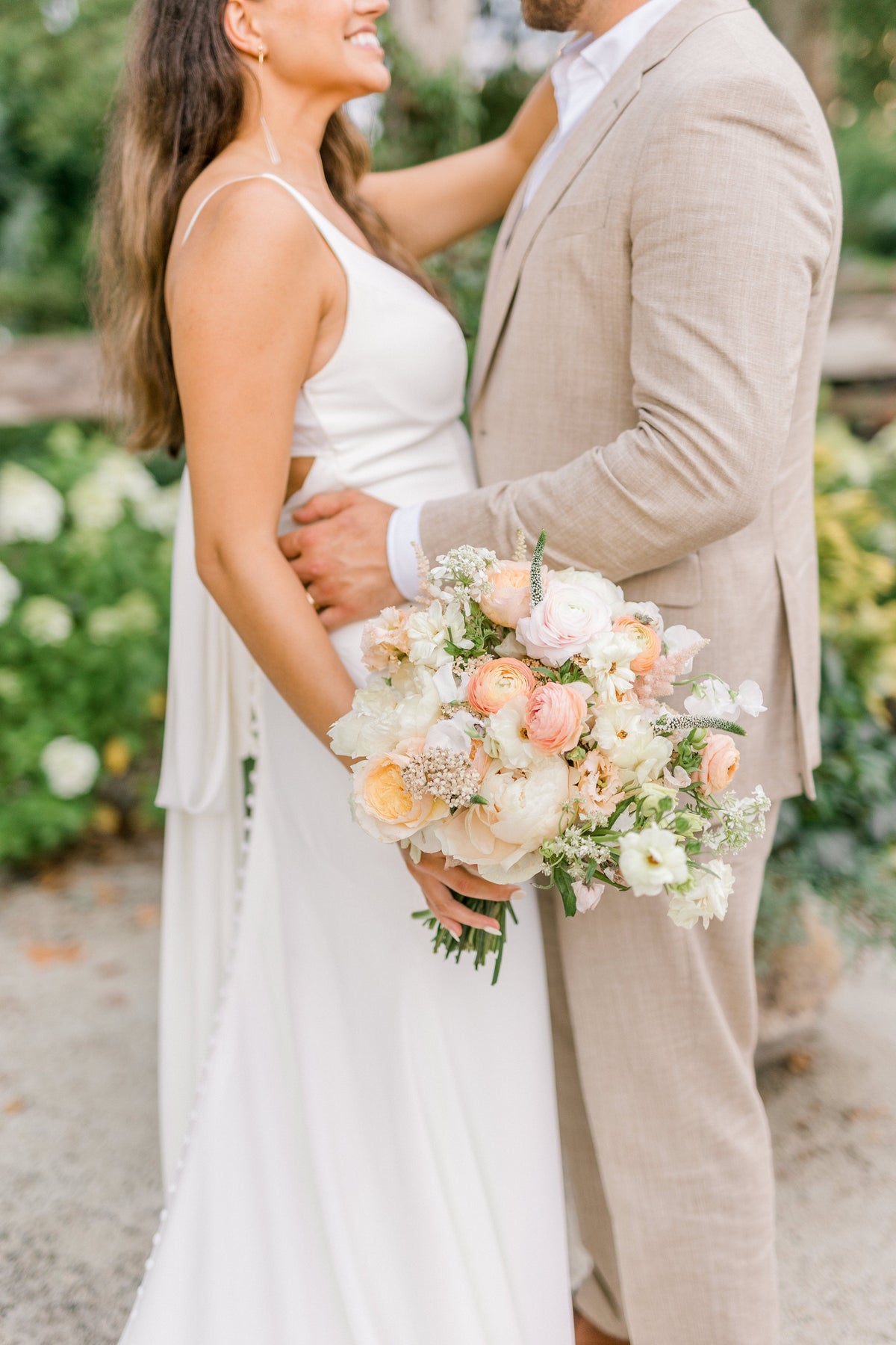 bride and groom facing each other holding a fresh orange, white and green bouquet 