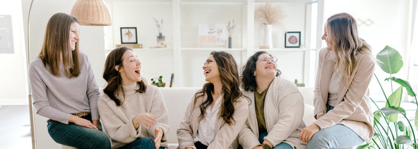 five women laughing with each other on a couch