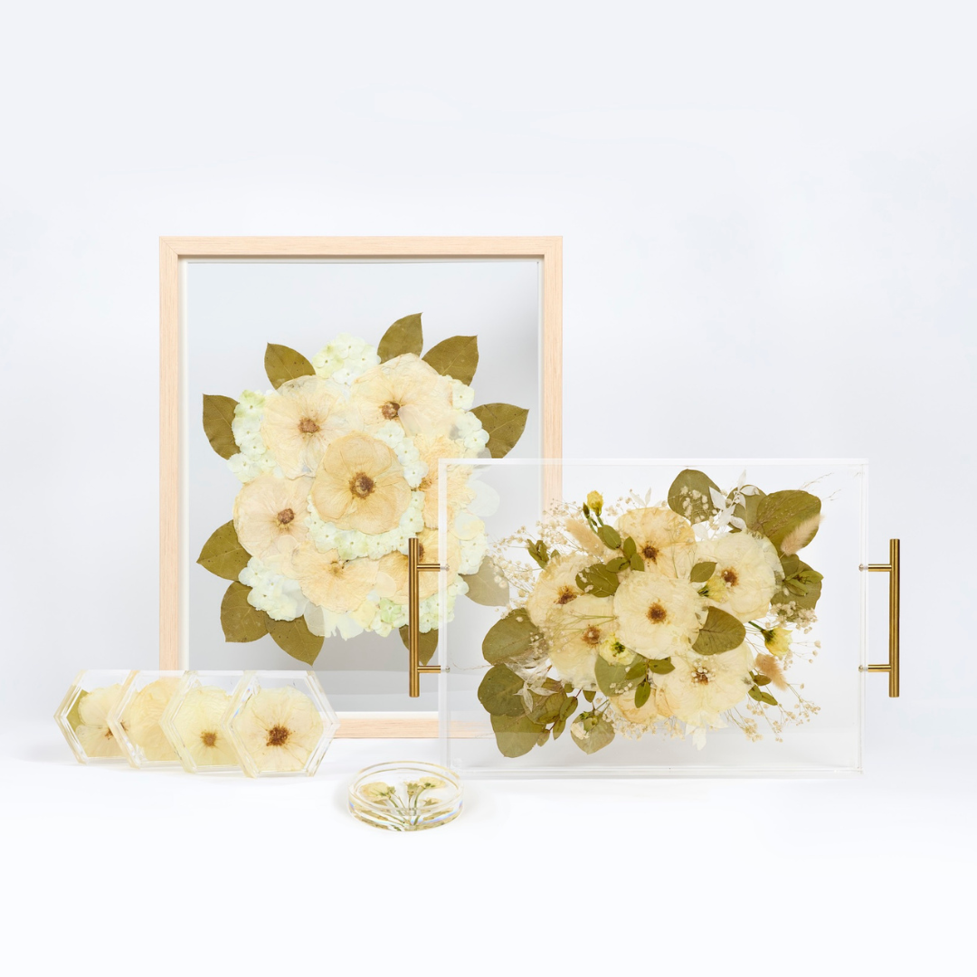 A collection of pressed wedding florals shown in a pressed flower frame, a floral serving tray, a set of pressed flower coasters, and a floral ring dish.