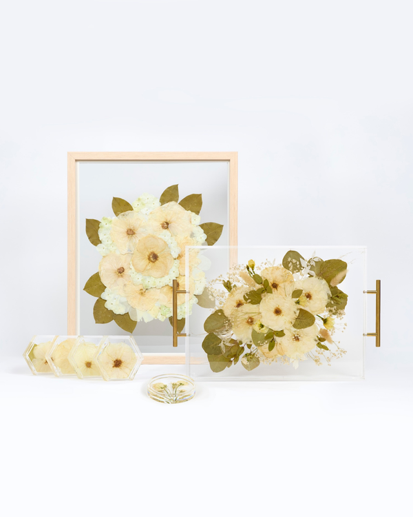 A collection of pressed wedding florals shown in a pressed flower frame, a floral serving tray, a set of pressed flower coasters, and a floral ring dish.