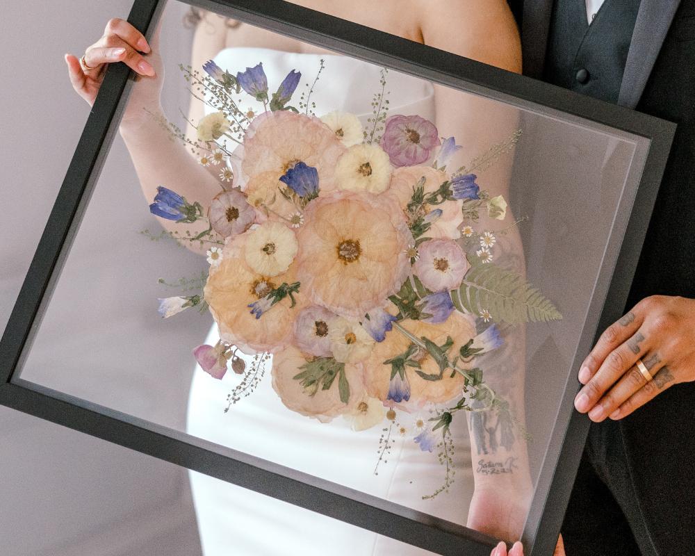 Pressed florals in a preservation frame - Preserved flowers by Element Design - a bride and groom holding their pressed wedding flowers in front of a window