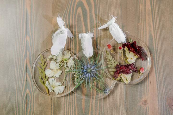 Three resin ornaments with blue, red, and white pressed florals laying against a wooden table.