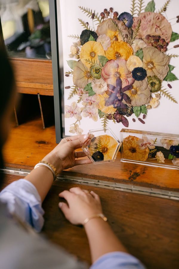 A pressed wedding bouquet sitting on a desk with smaller resin pressed flower items in front of it.
