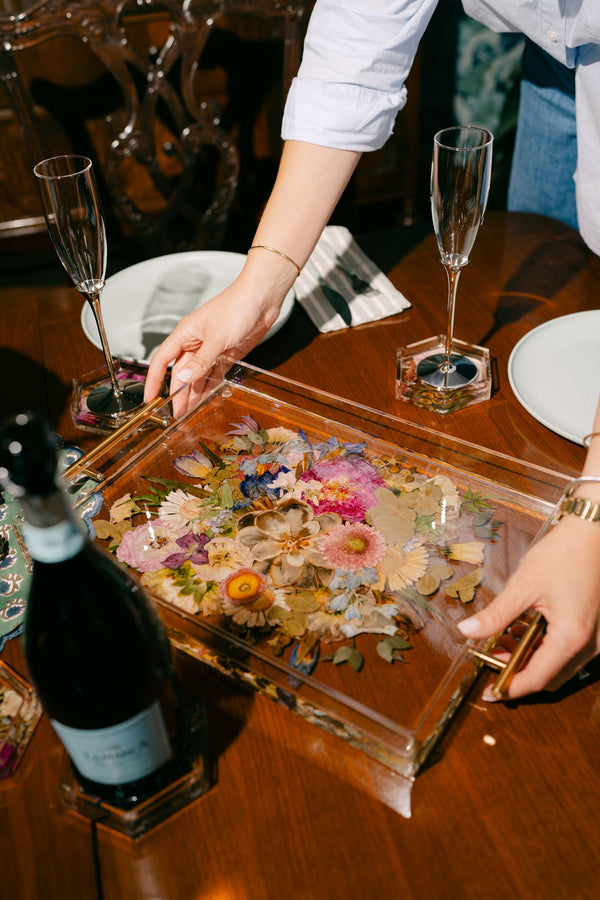 A woman sets down a pressed flower serving tray on a table set for entertaining.