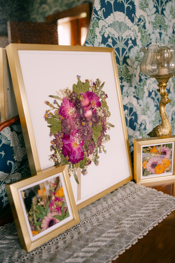 A pressed wedding bouquet in a large gold frame and two smaller mini pressed flower frames.