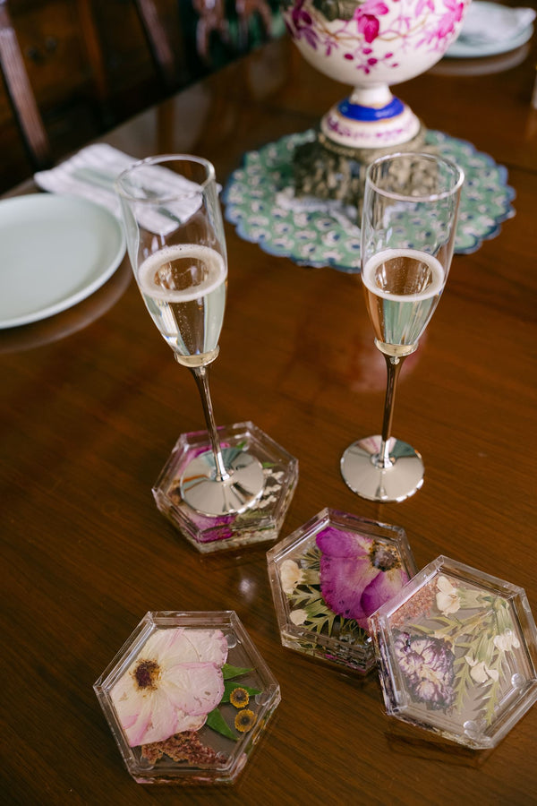 A set of pressed flower coasters on a table with a glass of champagne on top of one.