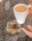 A cup of coffee is being set on top of a pressed flower coaster on a kitchen island. 