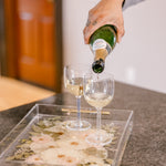 Pouring champagne into a custom pressed flower serving tray on a kitchen island. 