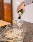 Pouring champagne into a custom pressed flower serving tray on a kitchen island. 