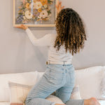 A bride hanging her bouquet preservation up on the wall in her home. These pressed florals feature wild flower tones and include pops of colors and greenery. 