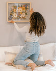 A bride hanging her bouquet preservation up on the wall in her home. These pressed florals feature wild flower tones and include pops of colors and greenery. 