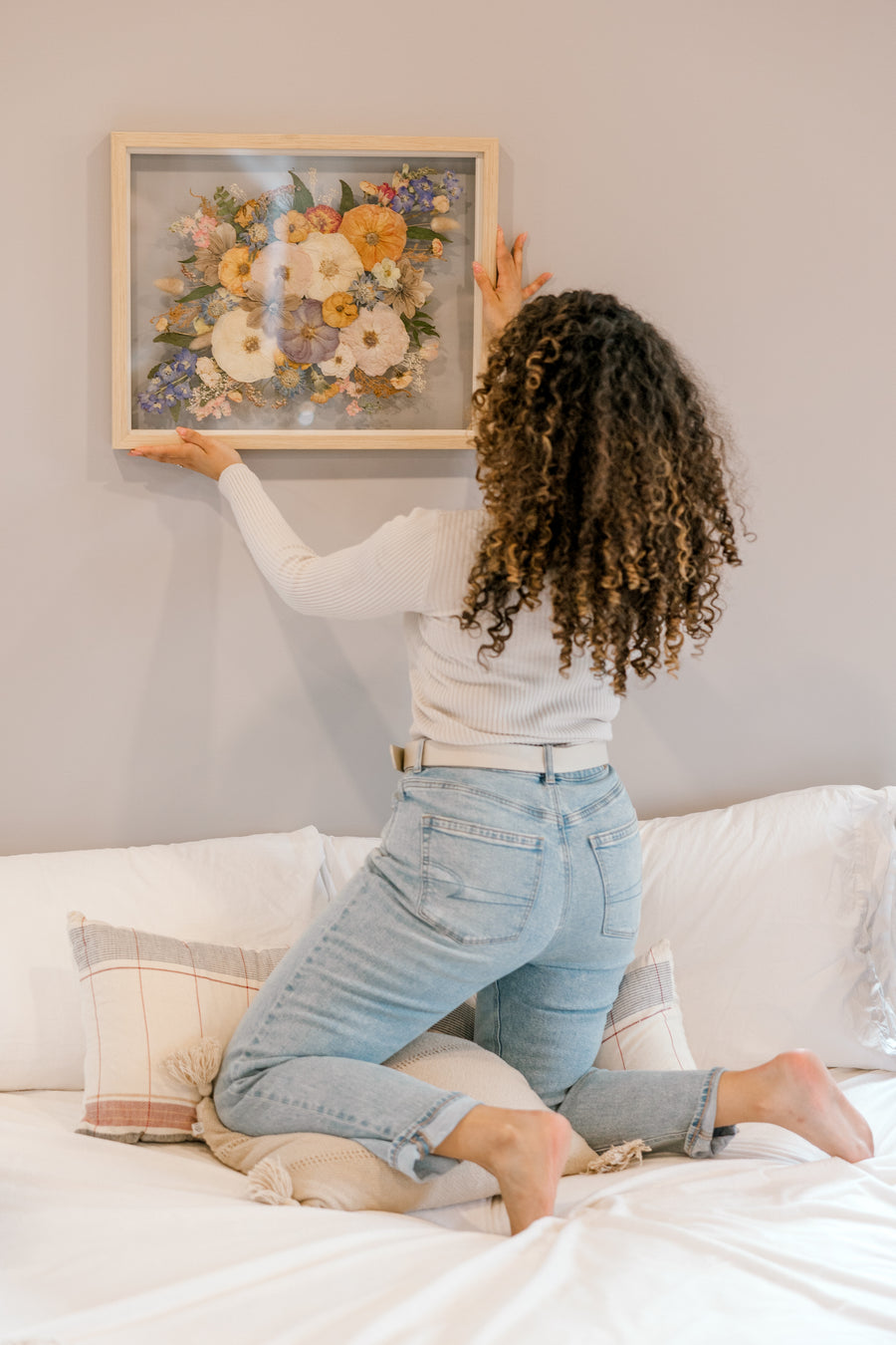 A bride hanging her bouquet preservation up on the wall in her home. These pressed florals feature wild flower tones and include pops of colors and greenery. 