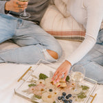 A couple happily uses their pressed floral serving tray while sitting on their bed.