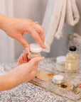 A pressed flower display tray is used as a dish to hold powder room beauty supplies while a woman prepares for the day.