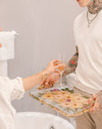 A pressed flower serving tray is used to serve a glass of champagne to a woman as she refreshes from the day. 