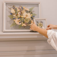 Two grey wood pressed floral frames are displayed on a mantle to be showcased in their home.