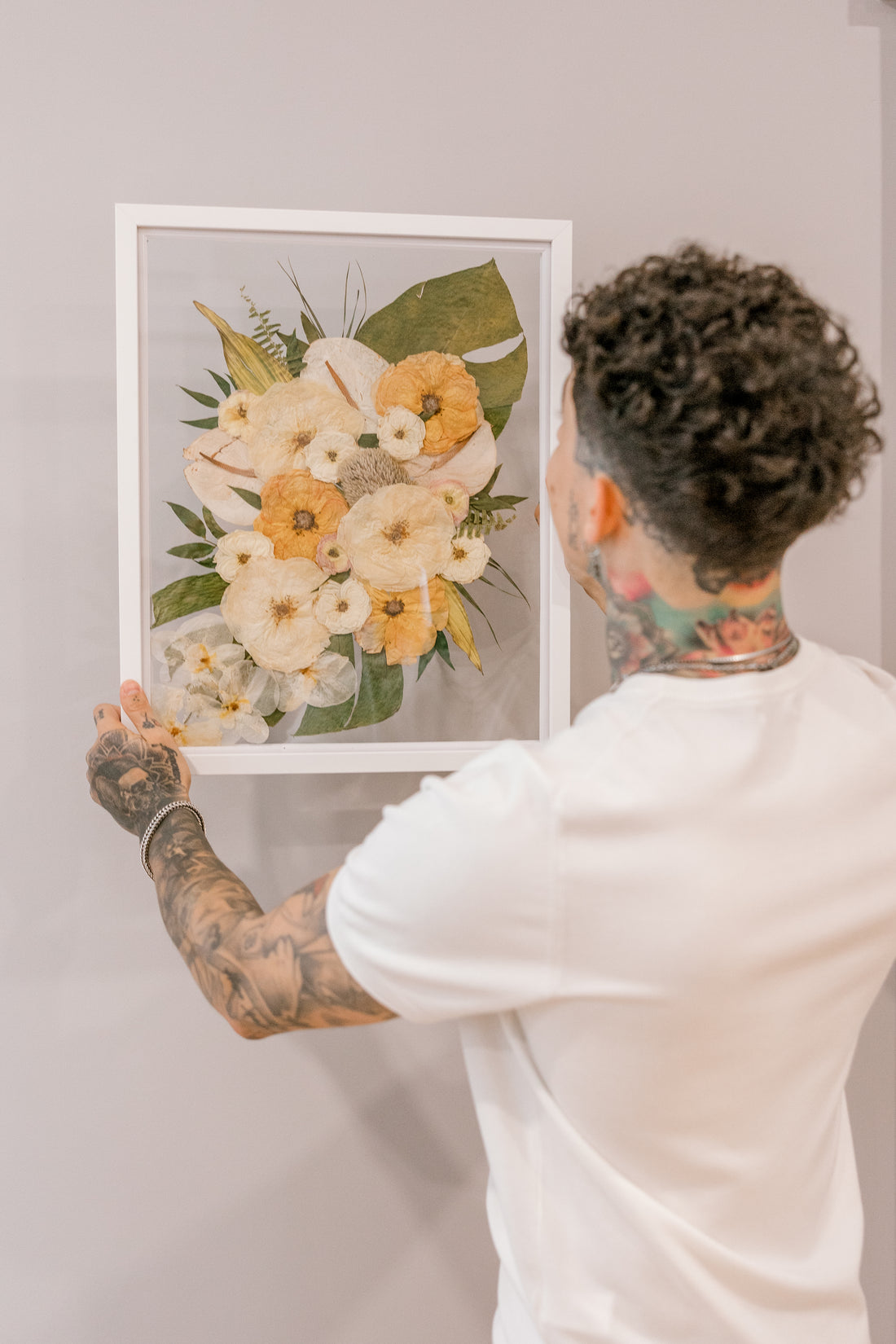 A groom hanging a bouquet preservation piece in his home that featured pressed tropical flowers such as preserved monstera leaves, pressed roses, and pressed orchids. 