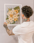 A groom hanging a bouquet preservation piece in his home that featured pressed tropical flowers such as preserved monstera leaves, pressed roses, and pressed orchids. 