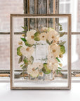 A beautiful bouquet preservation featuring white pressed roses and a preserved wedding invitation surrounded by pressed greenery in a barn wood frame.