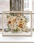 Pressed flowers and pressed florals in a natural wood float frame featuring pressed roses, pressed dahlias, pressed ranunculus, and pressed greenery. 