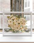 A beautiful pressed white bouquet with pops of greenery featured in a brightly lit window sill. Proudly designed by Element Preservation.