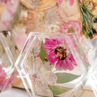 A hexagon shaped pressed floral ring dish sits aside a background of pressed and framed florals. 