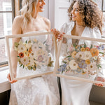 Two brides happily holding their pressed flower preservation pieces, smiling at each other and the lifetime of memories they will hold. 