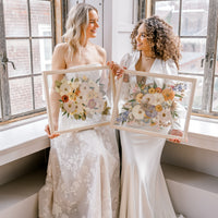 Two brides happily holding their pressed flower preservation pieces, smiling at each other and the lifetime of memories they will hold. 