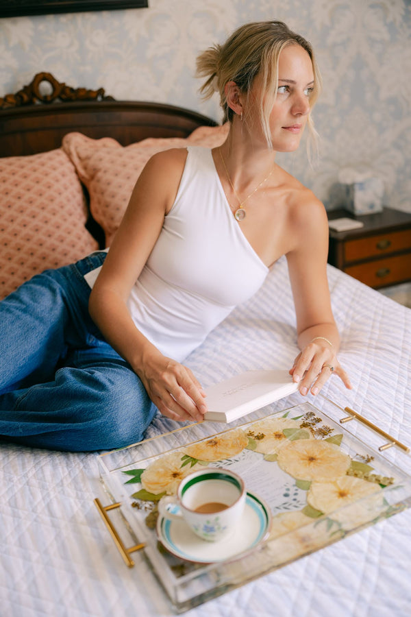 A woman relaxing on her bed with her pressed flower tray and a wedding bouquet locket.