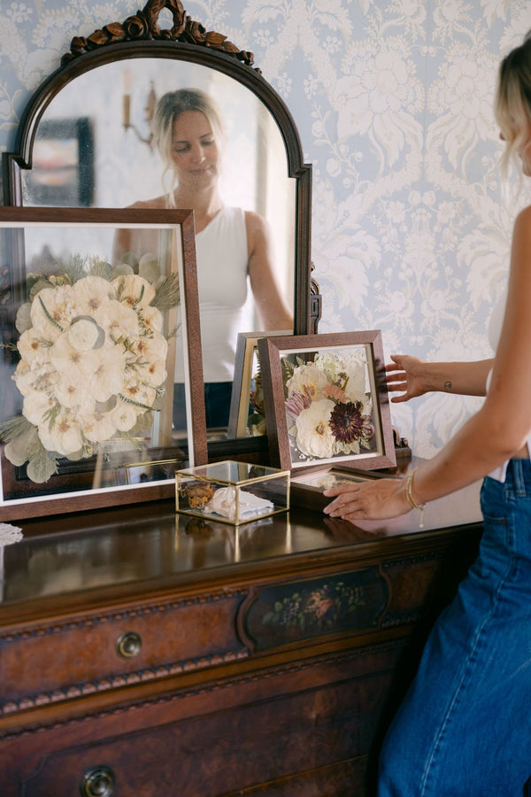 Two bouquet frames setting on an antique dresser with a woman softly admiring her frames.