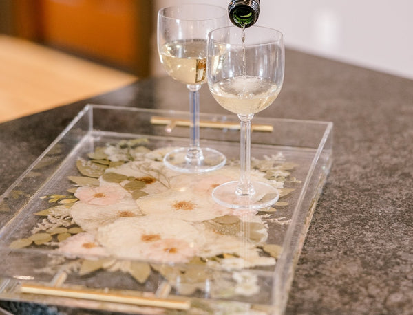 A preserved flower serving tray sits on a table with drinks being poured on it.