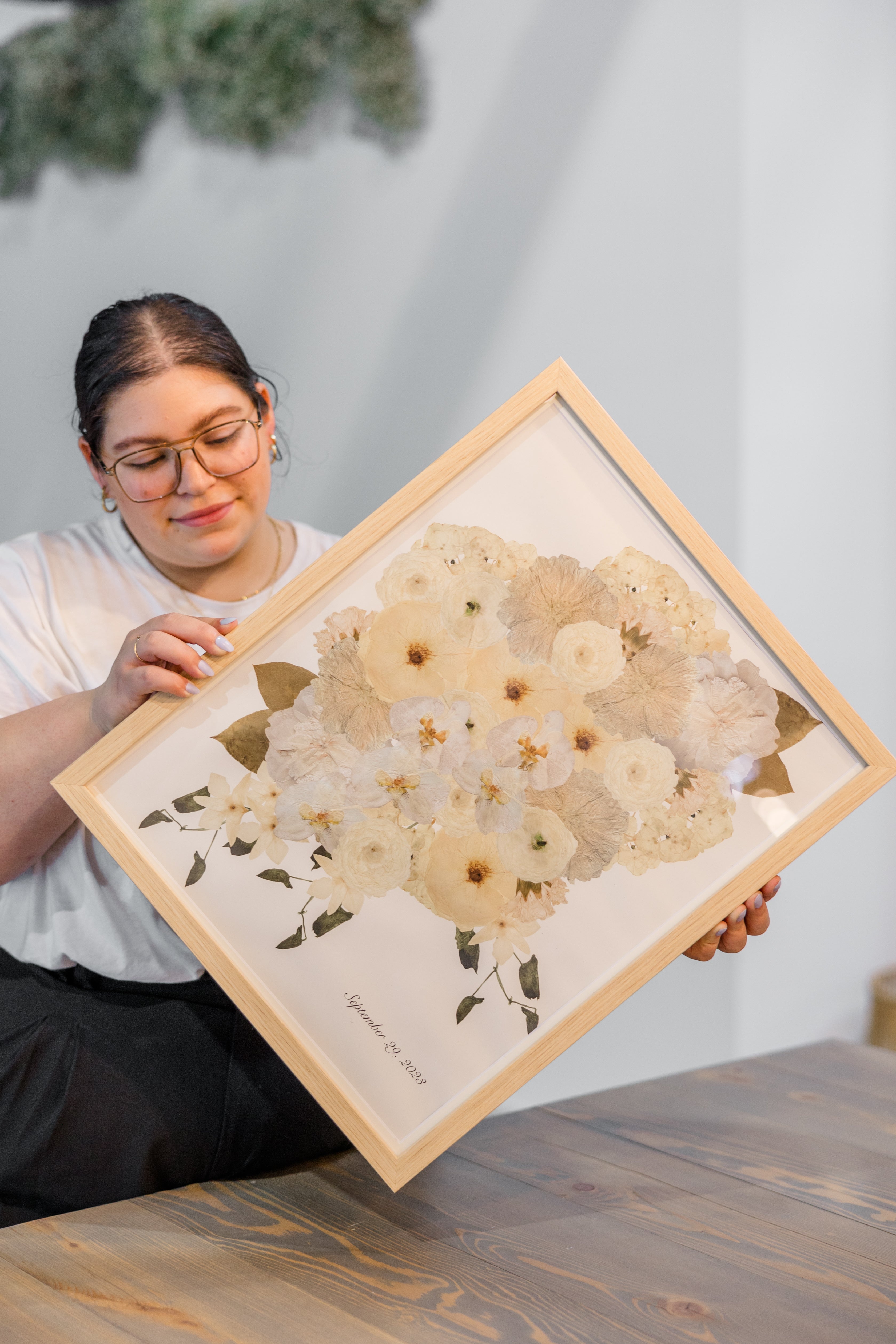 A woman holding a large frame with digitized white pressed florals designed into a custom frame