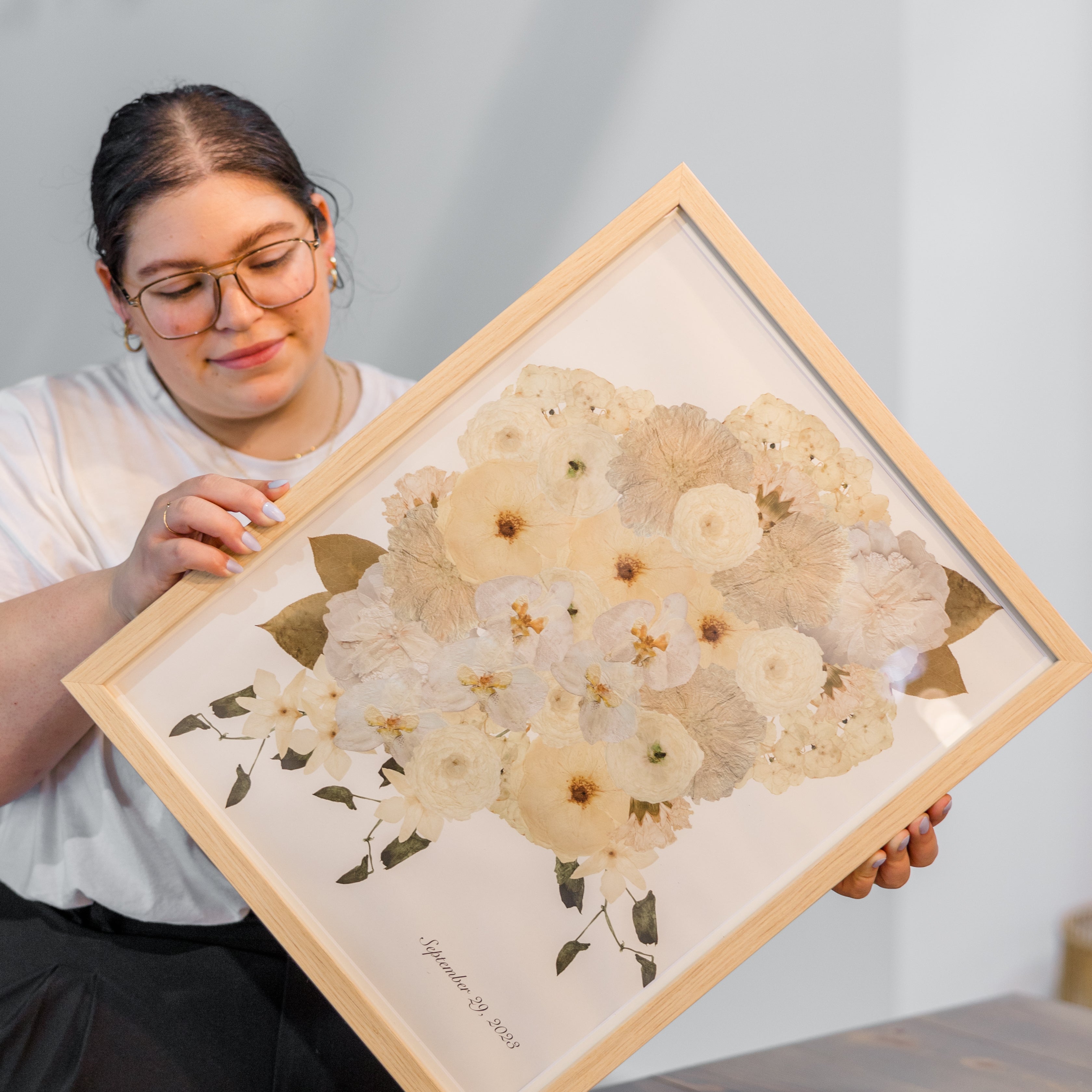  A woman holding a large frame with digitized white pressed florals designed into a custom frame